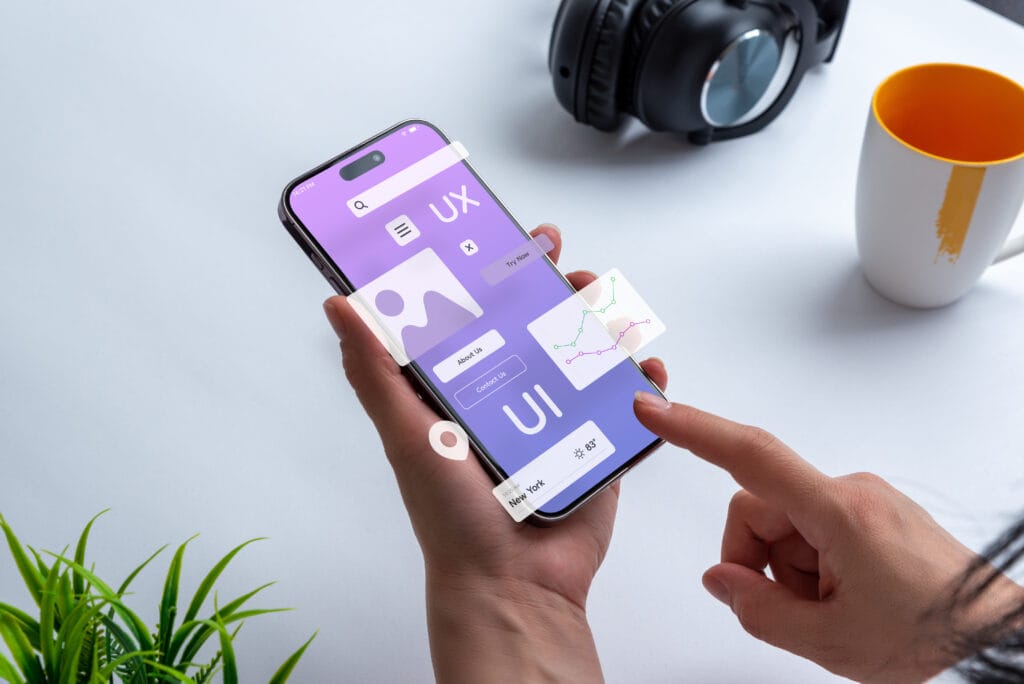 Dłonie trzymające smartfon z wizualizacją interfejsu aplikacji mobilnej UI/UX.